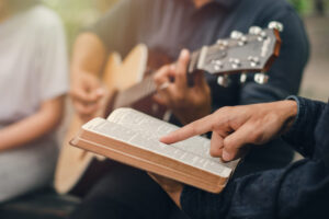 A young boy reads the Bible while his friend plays the guitar. w